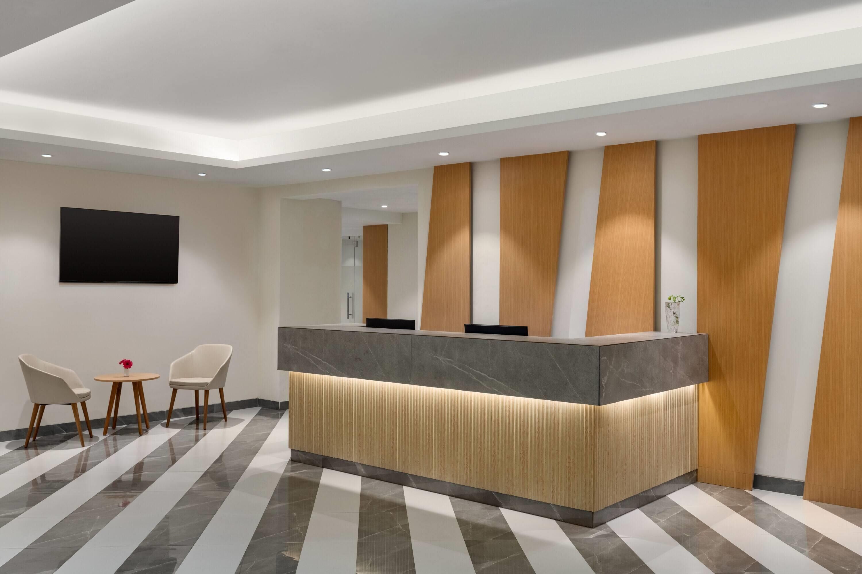 A reception area with a modern design, featuring a reception desk, two chairs, and a small table with a vase.