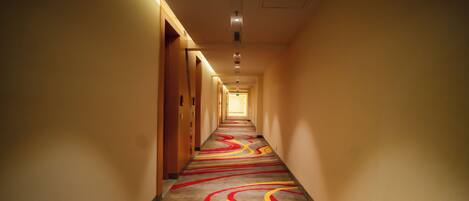 A long, narrow hotel corridor with a patterned carpet and recessed lighting.