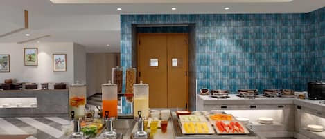 A modern hotel lobby with a buffet area featuring various food items and beverages.