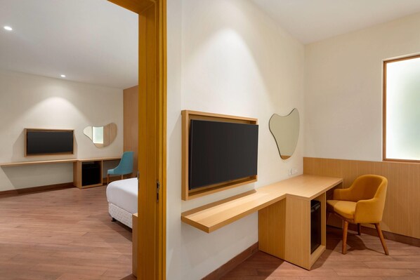 Una habitación de hotel moderna con una cama, un escritorio con una computadora, una silla y dos televisores instalados en la pared.