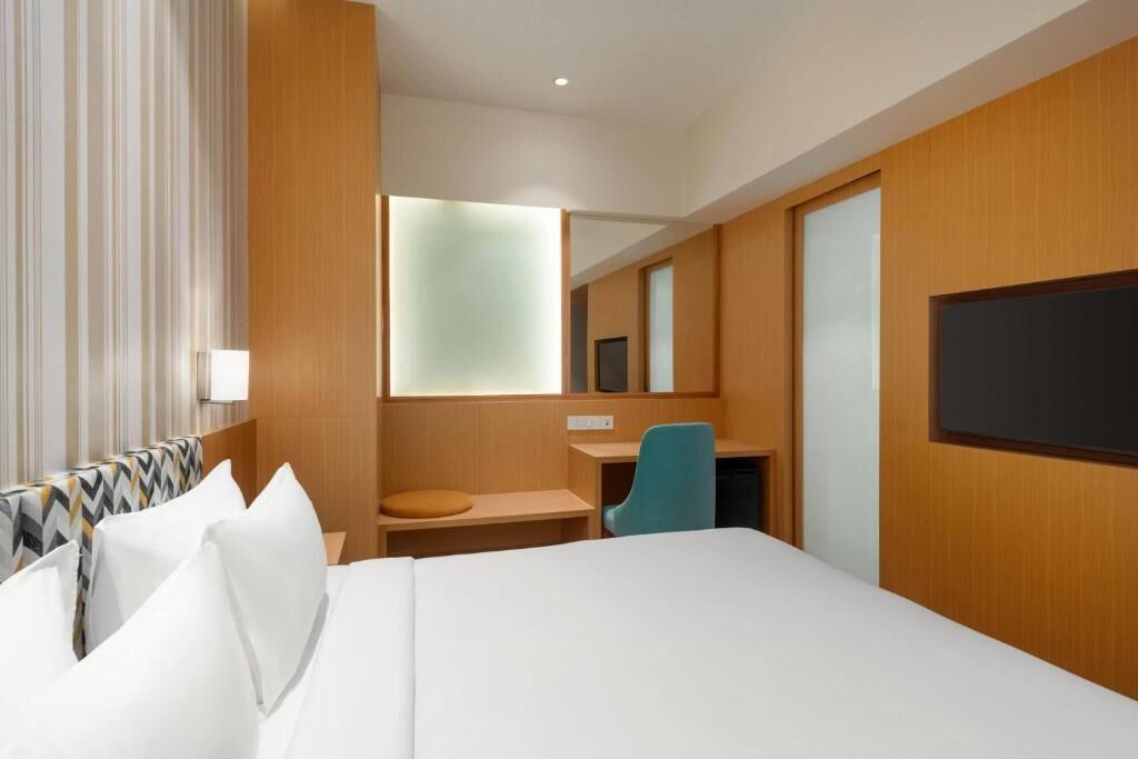 A hotel room with a bed, a desk, a chair, a television, and a mirror.
