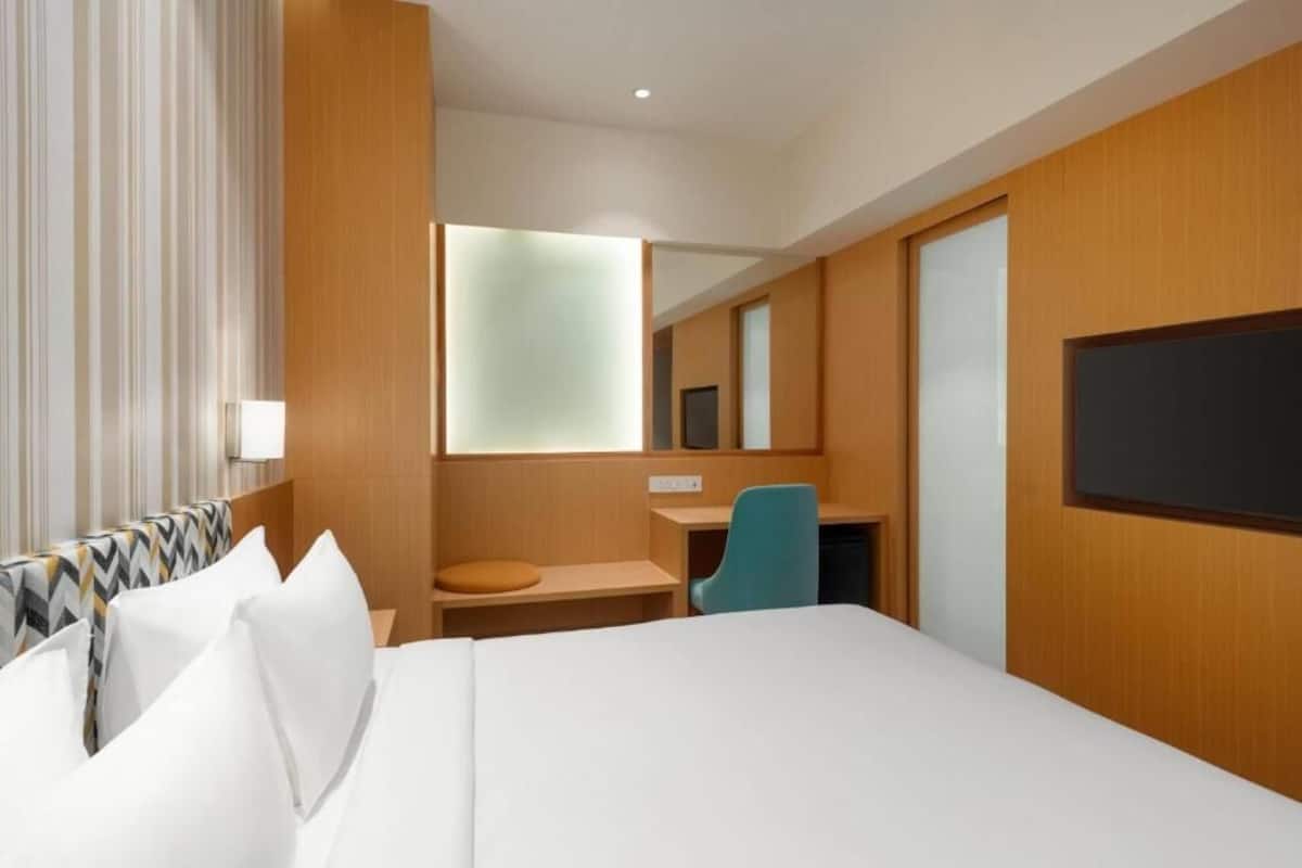 A hotel room with a bed, a desk, a chair, a television, and a mirror.