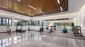 Un gimnasio amplio con equipo de ejercicio, ventanas grandes y piso pulido.