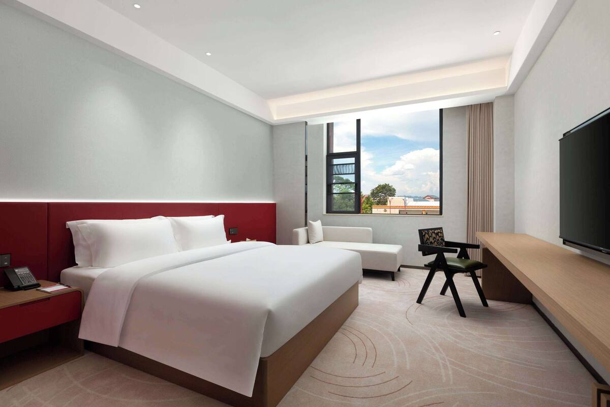 A modern hotel room with a large bed, a seating area, a desk, and a TV.