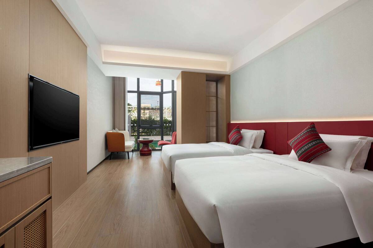 A hotel room with two beds, a TV, and a view of the outdoors.