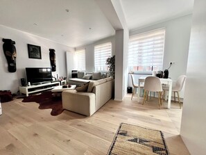 A modern living room with a sofa, TV, and dining area with chairs and a table. - Midi Station - 6 pers comfort (Brussels)