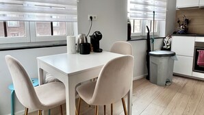 Una cocina moderna con una mesa y sillas blancas, una tetera y un cubo de basura.