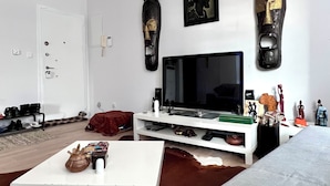 Un salón moderno con televisor de pantalla plana, mueble blanco para entretenimiento y objetos decorativos.