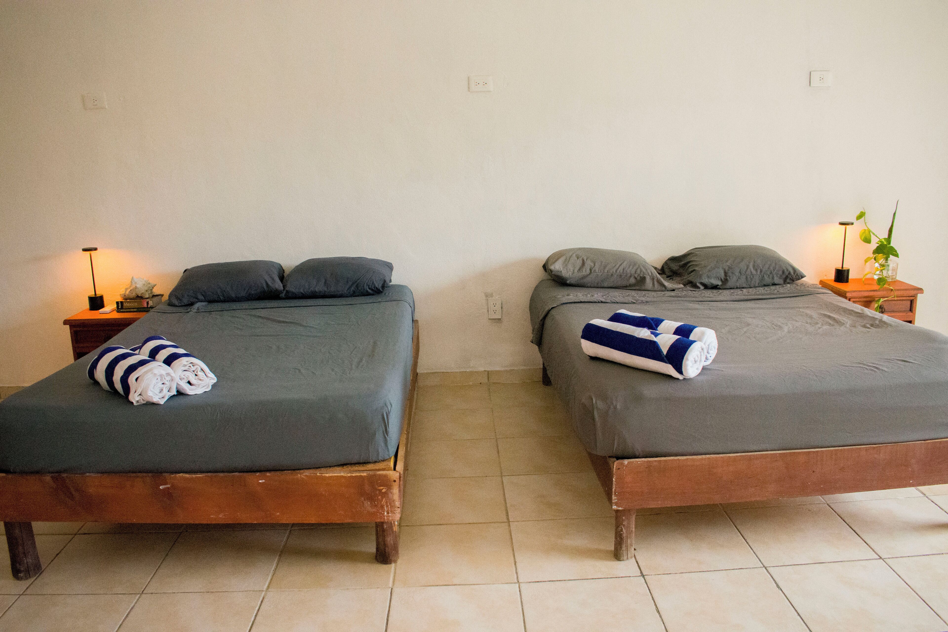 Two single beds with grey linens, wooden headboards, and bedside tables with lamps.