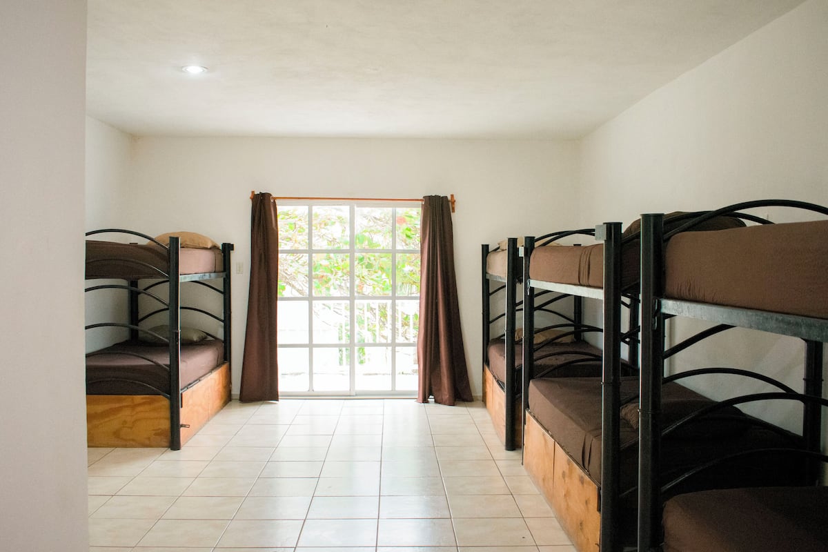 A room with bunk beds, a large window with curtains, and tiled flooring.