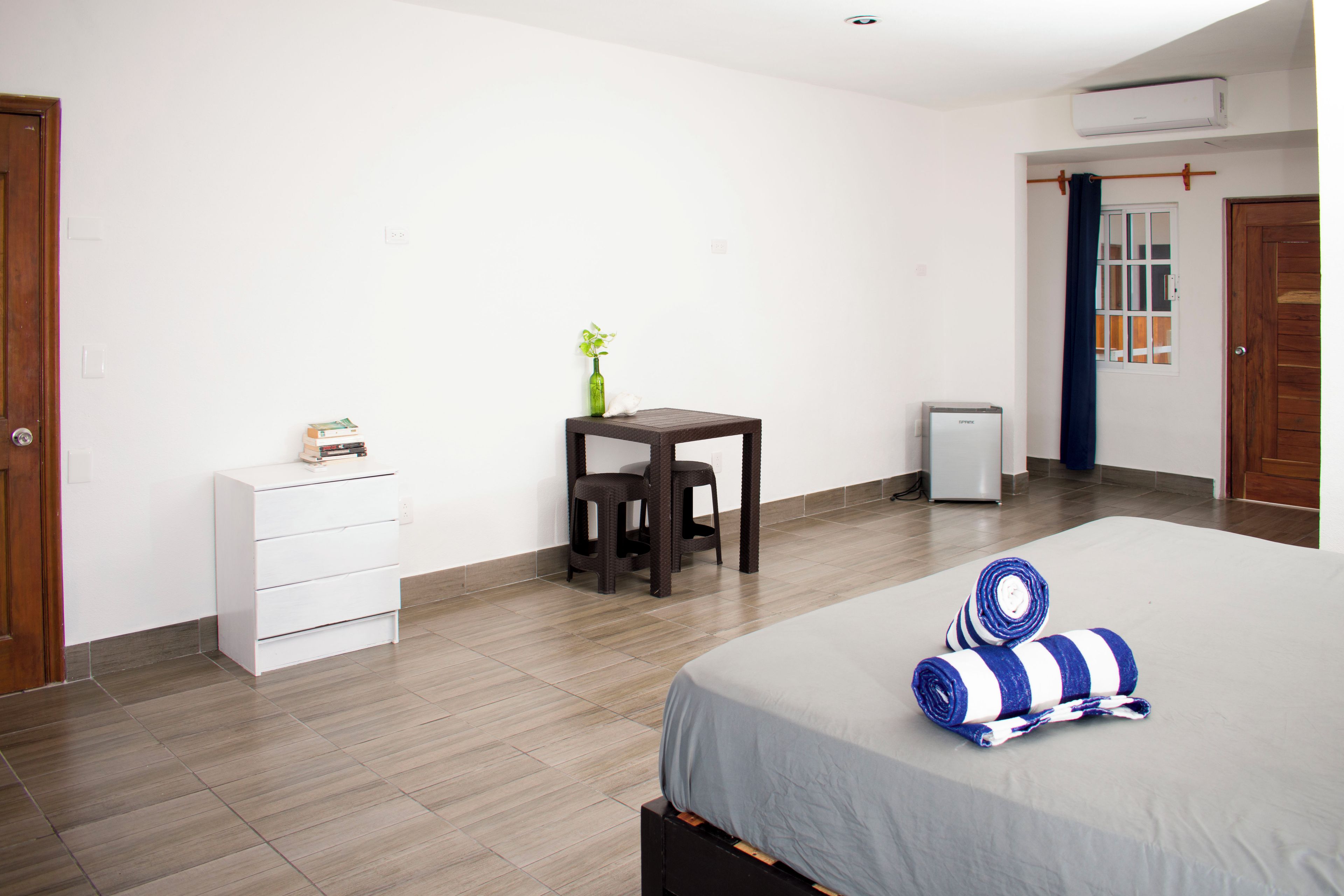 A hotel room with a bed, a small table with a plant, a white dresser, and a door.