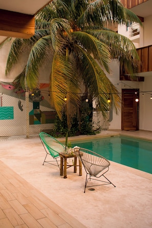 A pool area with a palm tree, two chairs, and a small table. - Balu Hotel (Isla Mujeres)