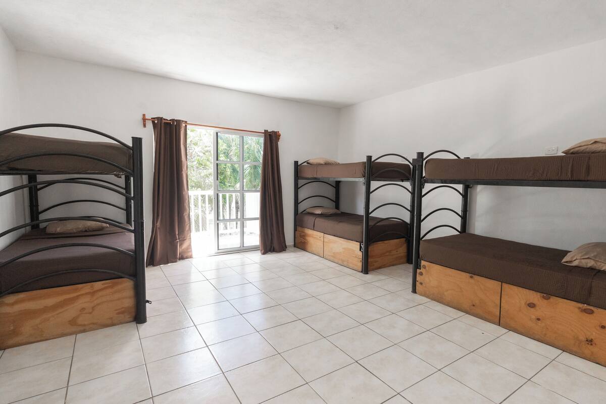 A dormitory room with bunk beds, a sliding glass door leading to a balcony, and tiled flooring.
