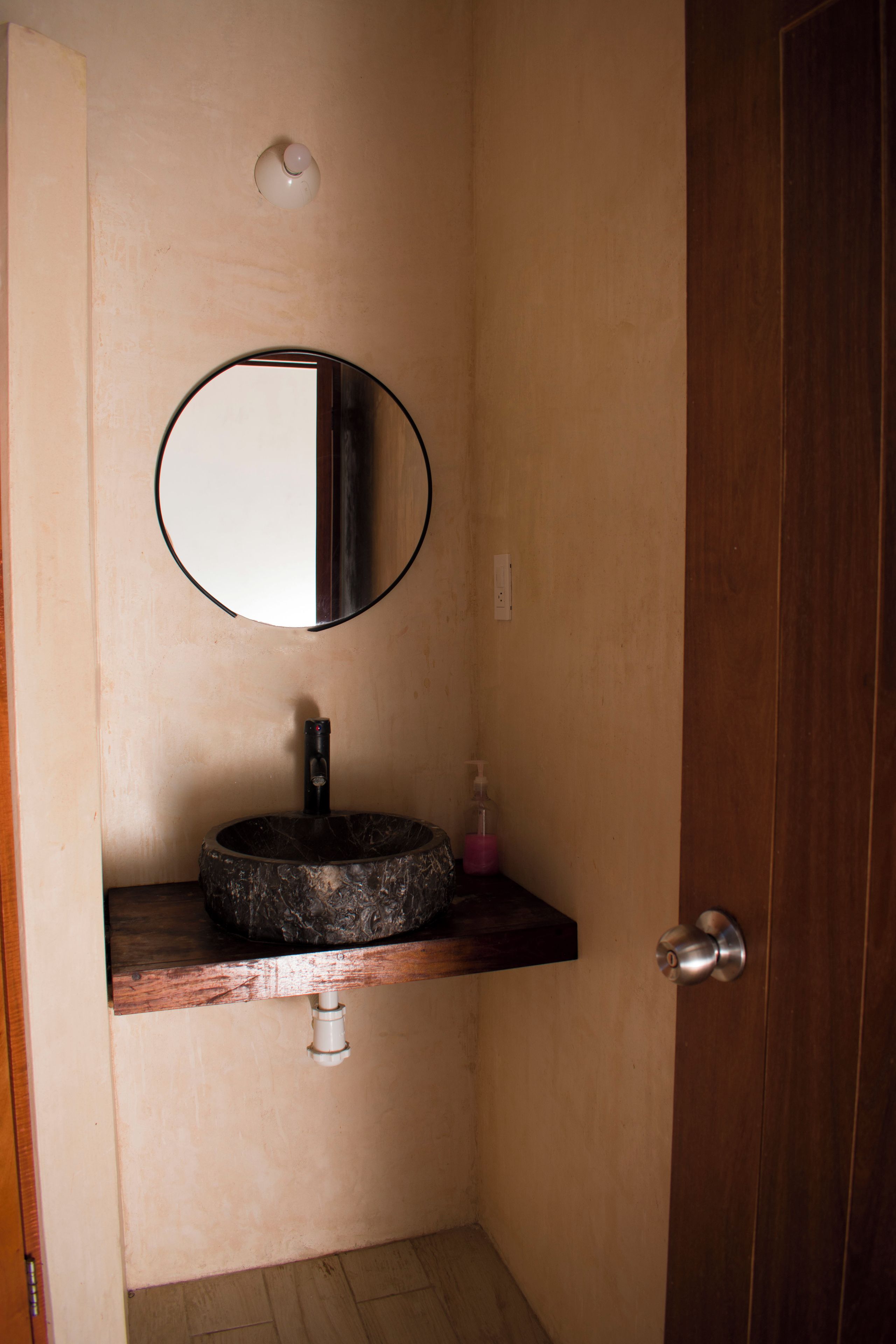 A bathroom with a round mirror, a sink with a marble-like countertop, and a wooden door.
