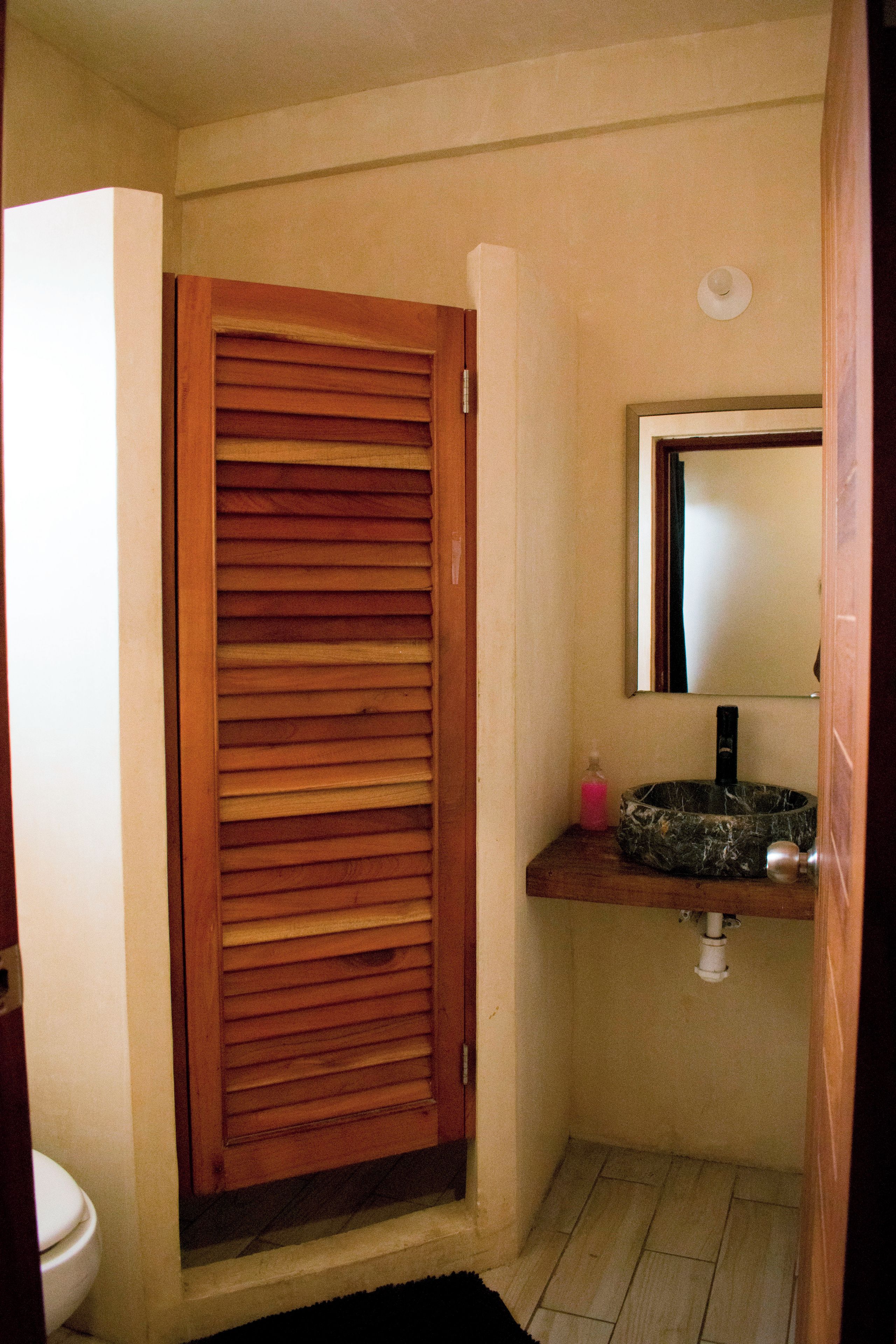 Un baño con puerta de madera, un lavabo con encimera de mármol y un espejo encima.