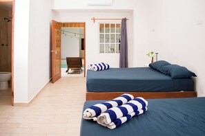 A bedroom with two beds, a wooden door, a window with curtains, and a small plant. - Balu Hotel (Isla Mujeres)