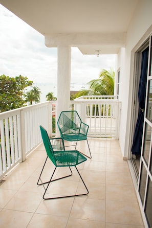 A balcony with two green chairs, a white railing, and a view of the sea. - Balu Hotel (Isla Mujeres)