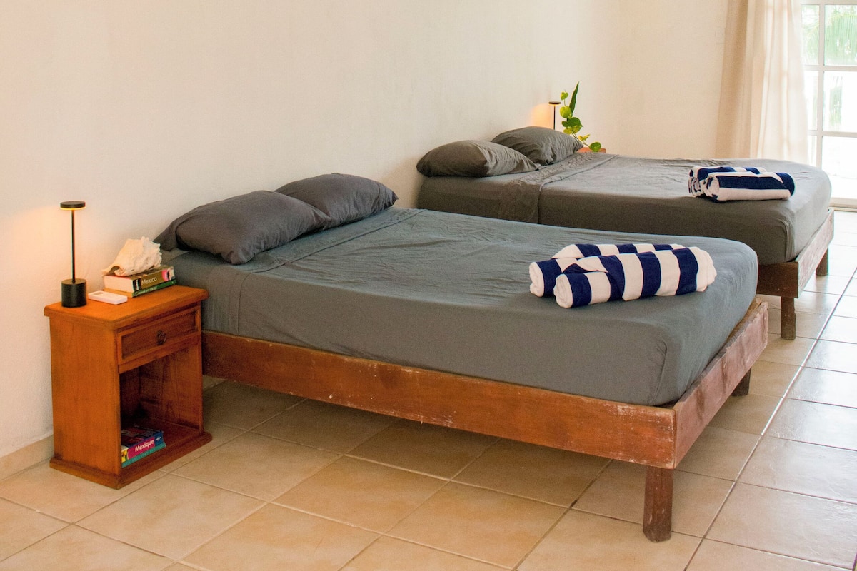 A room with two beds, a nightstand, and a window with curtains.