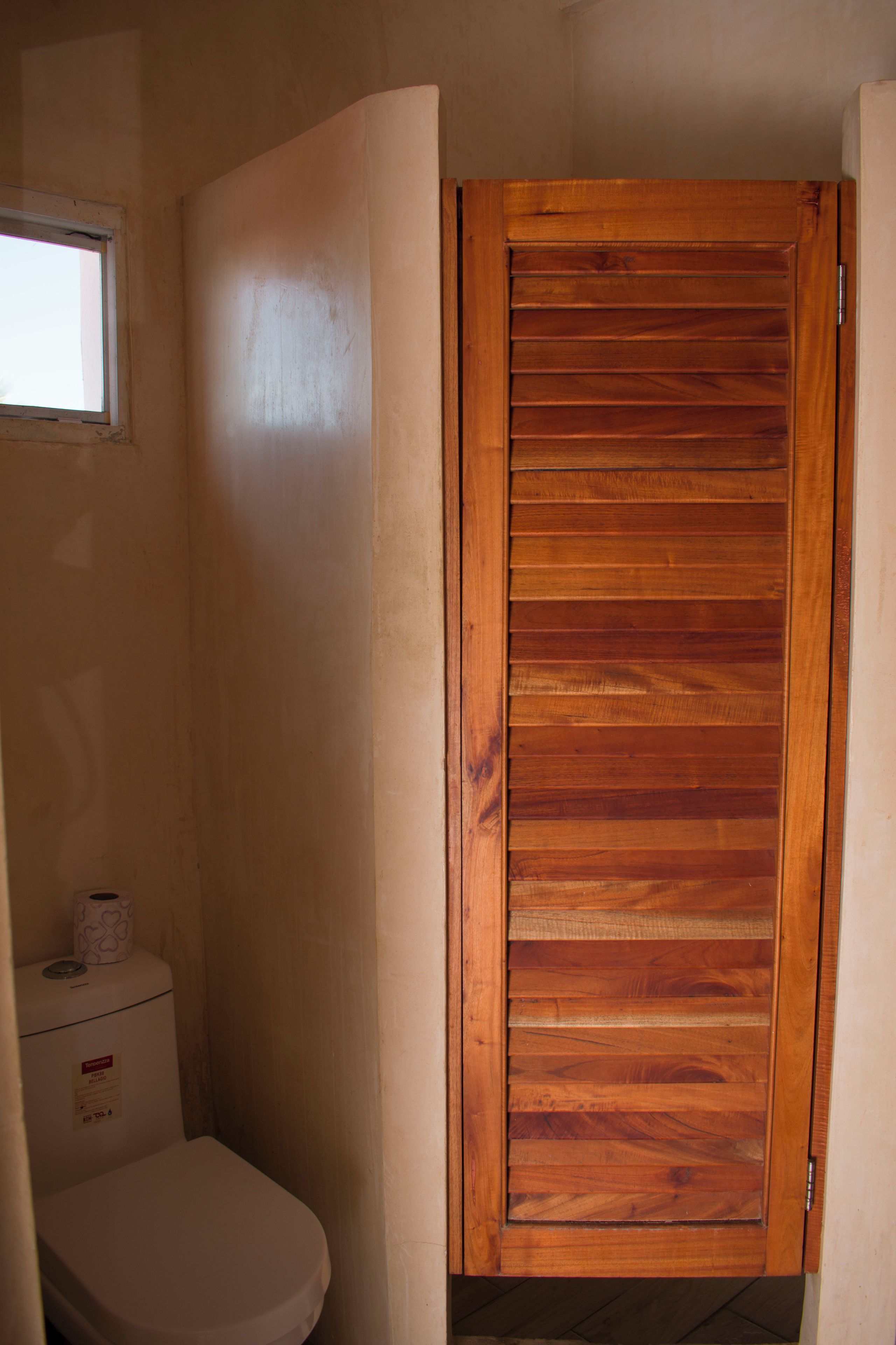 Ein kleines Badezimmer mit Holztür, Toilette und Fenster.