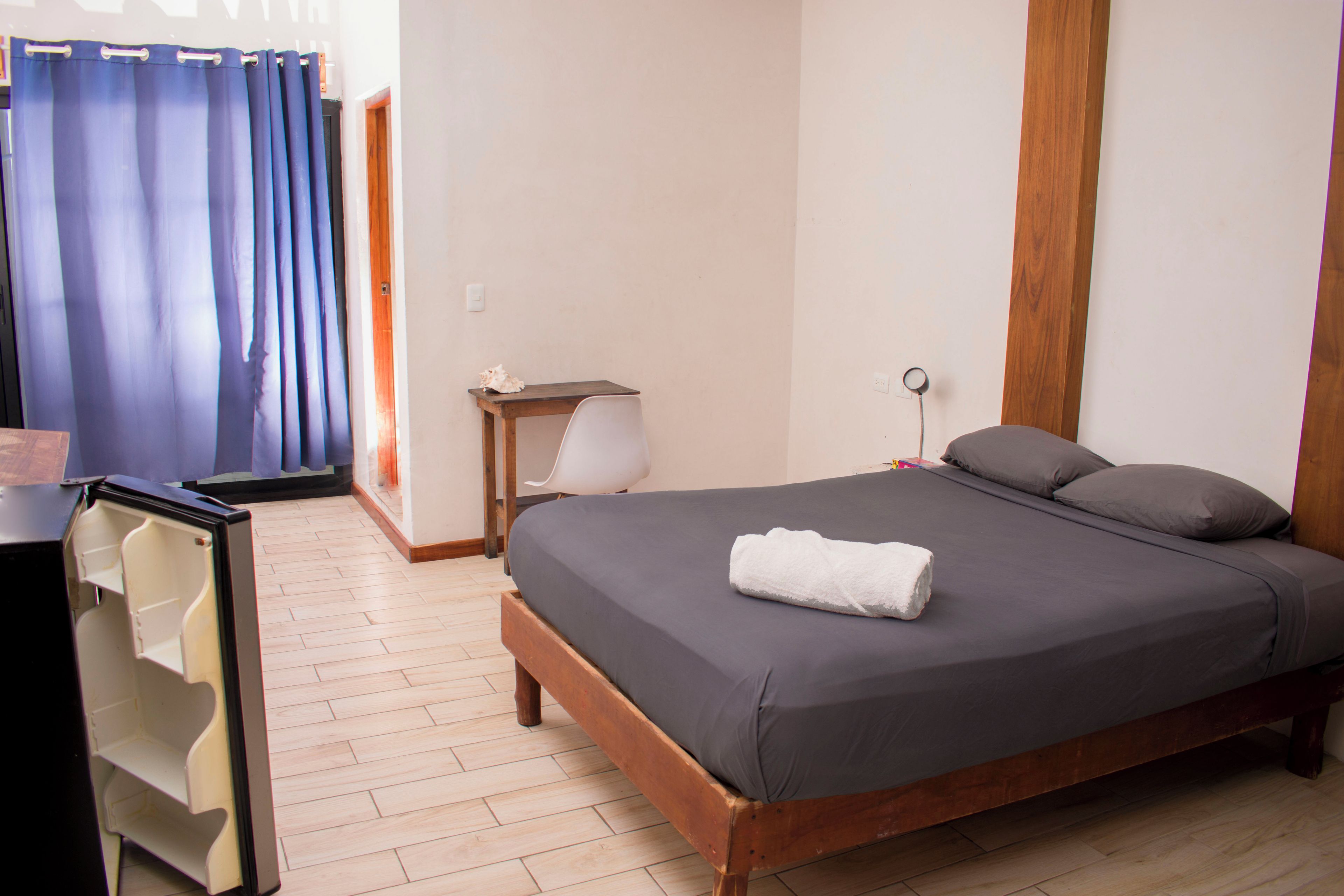 A bedroom with a wooden bed, a nightstand, a lamp, and a blue curtain.