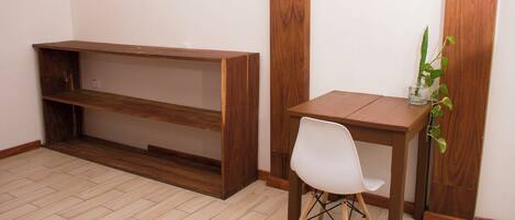 Une pièce avec un bureau et une chaise en bois, une petite plante en pot et une étagère adossée au mur.