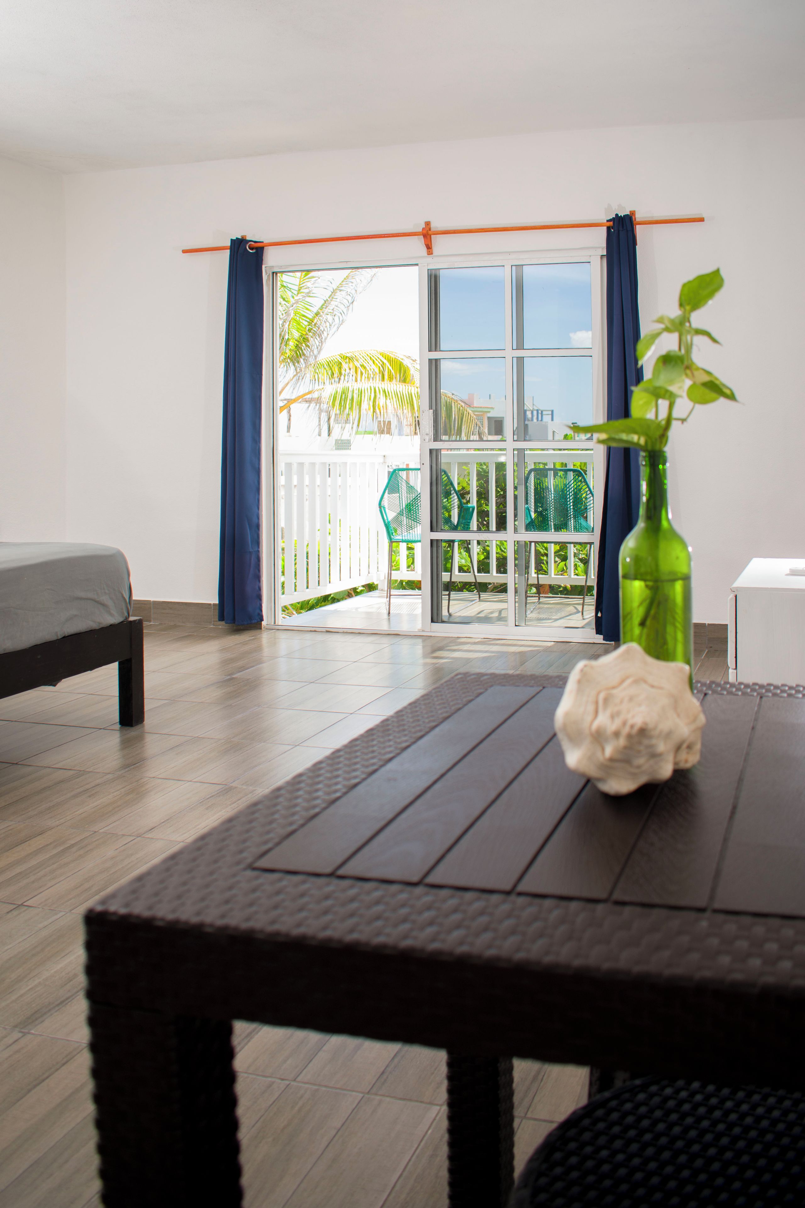 Una habitación con una cama, una mesa con una planta y vistas a un balcón con barandilla.