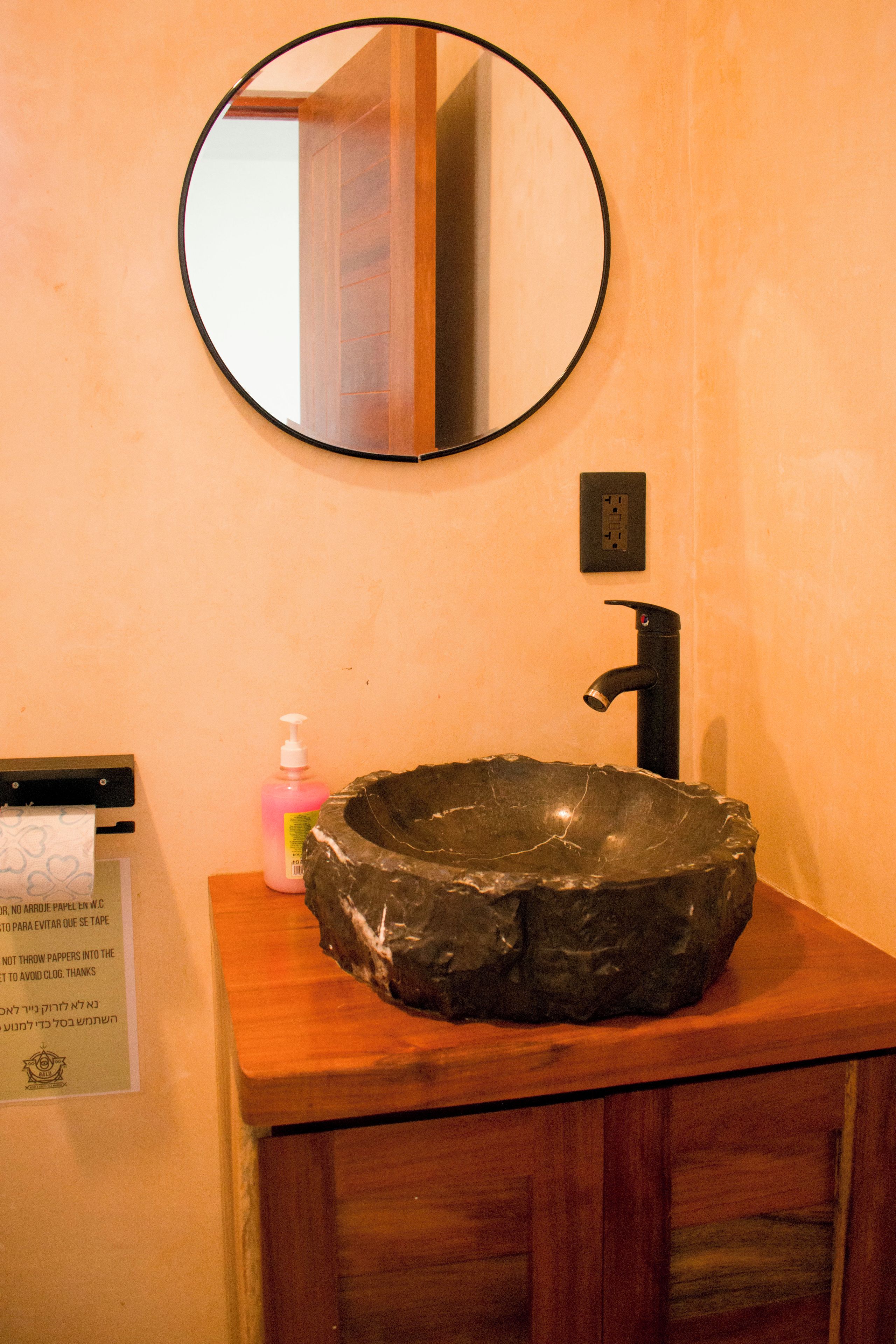 A bathroom with a round mirror, a black sink, and a wooden cabinet.