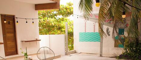 A swimming pool with two people in the water, surrounded by a wooden deck, chairs, and a fence.