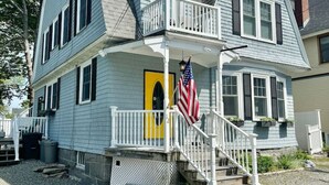 Une maison à deux étages avec un porche à l’avant, une porte jaune et un drapeau américain.