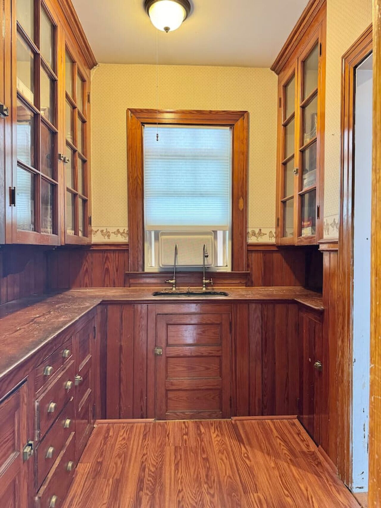 A compact kitchen with wooden cabinets, a built-in sink, and a window with blinds.