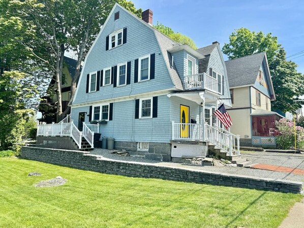 A two-story house with a front porch, a small deck, and a stone retaining wall.