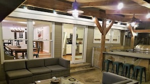 Un espace de vie extérieur comprenant un canapé, des fauteuils, une table basse et un coin bar avec des tabourets.