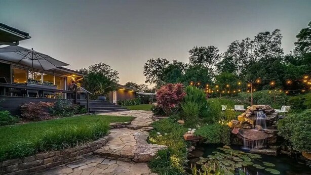 A stone pathway leading to a pond with a waterfall and surrounding greenery. - The Only Private Pickleball Vacation in Dallas! (Dallas)