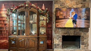 A living room with a wooden bookcase, a fireplace, and a television displaying 'Beauty and the Beast'.