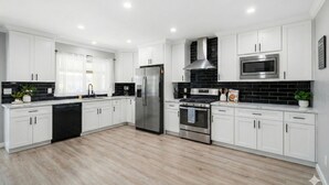 A modern kitchen with white cabinets, stainless steel appliances, and a black tiled backsplash.