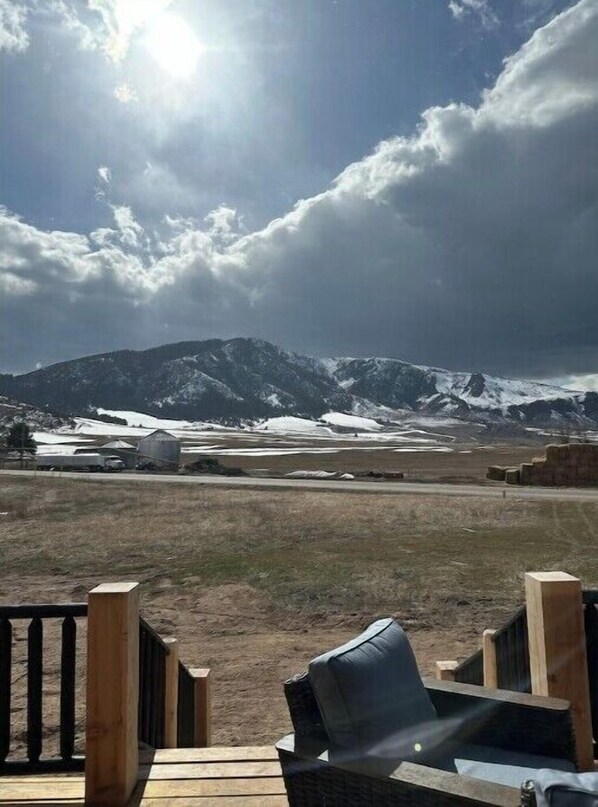 Eine Holzterrasse mit Stuhl und Tisch, mit Blick auf eine verschneite Berglandschaft unter blauem Himmel.