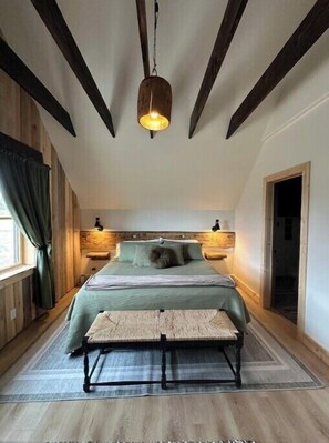 Ein Schlafzimmer mit Bett, Nachttischen, einer Bank, einer Pendelleuchte und Holzbalken an der Decke.