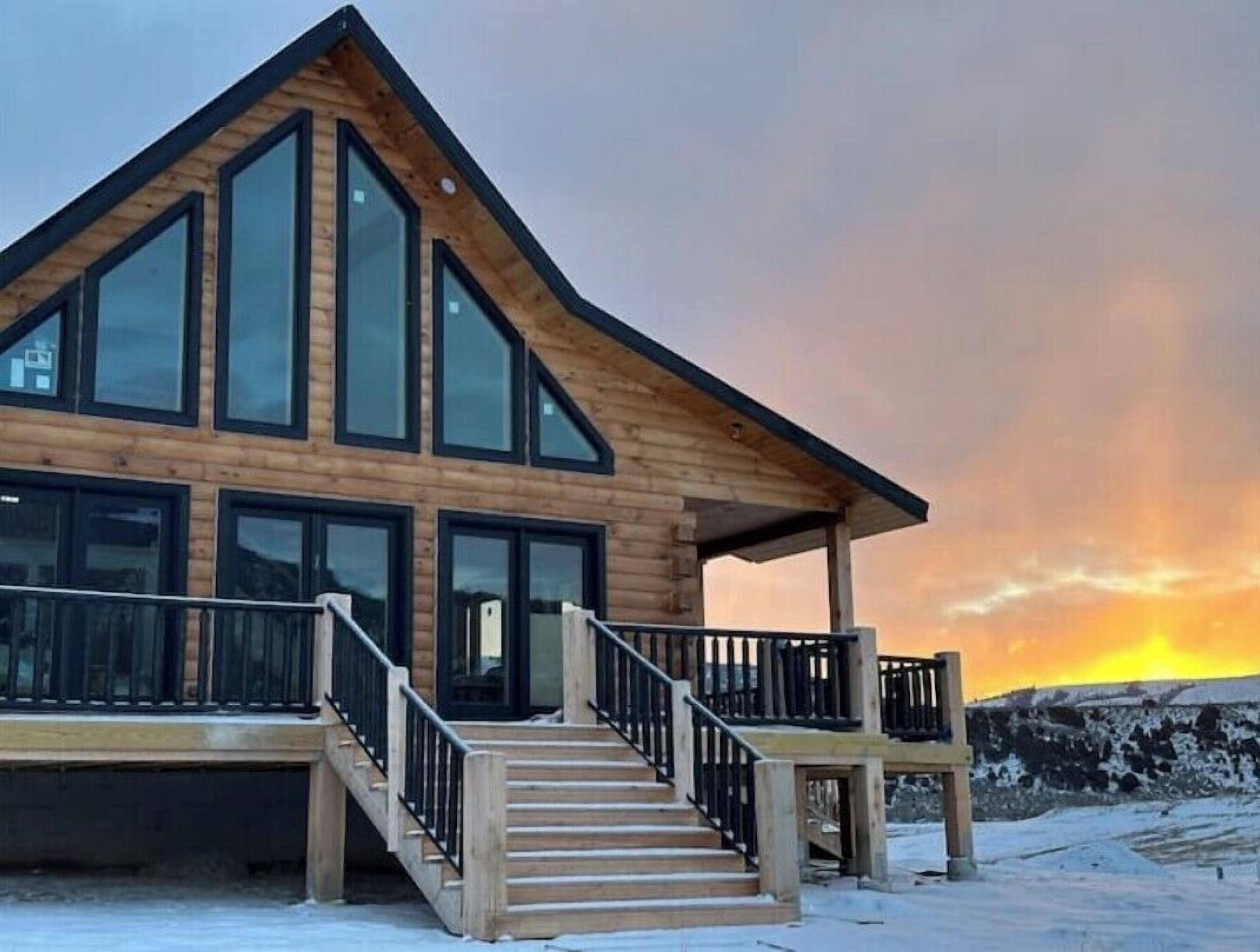 Une maison en rondins moderne, dotée de grandes fenêtres et d’une façade en bois.