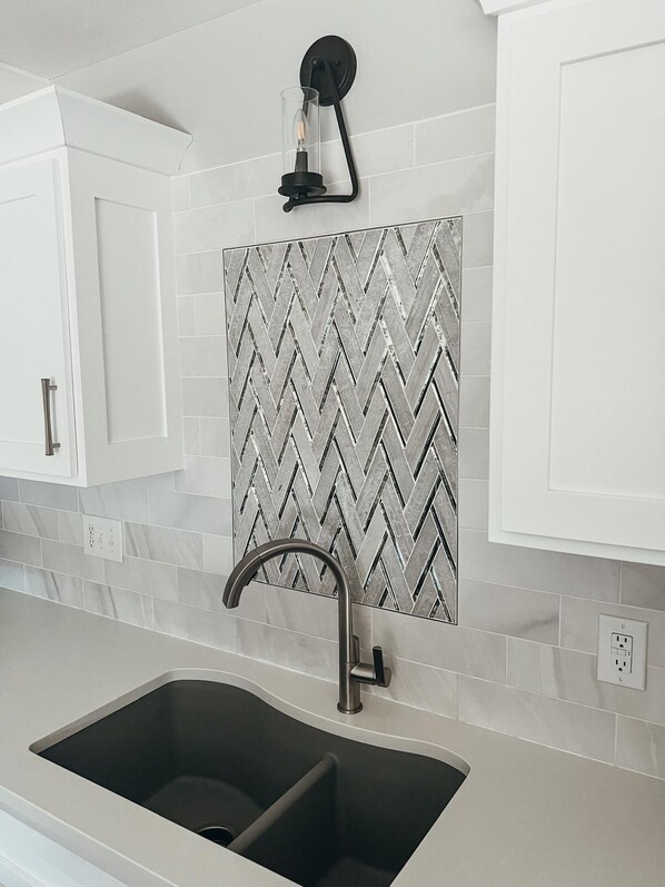 A kitchen with a double sink, white cabinets, a herringbone tile backsplash, and a pendant light above the sink. - Renovated Ranch: 3BDRM 2BATH with King Bed, En-Suite, Sleeps 6, Hot Tub & more! (Newburgh)