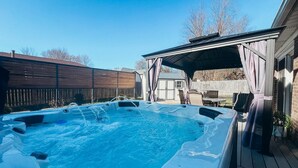 Ett bubbelbad på ett trädäck med ett takförsett sittområde och ett trästaket i bakgrunden.