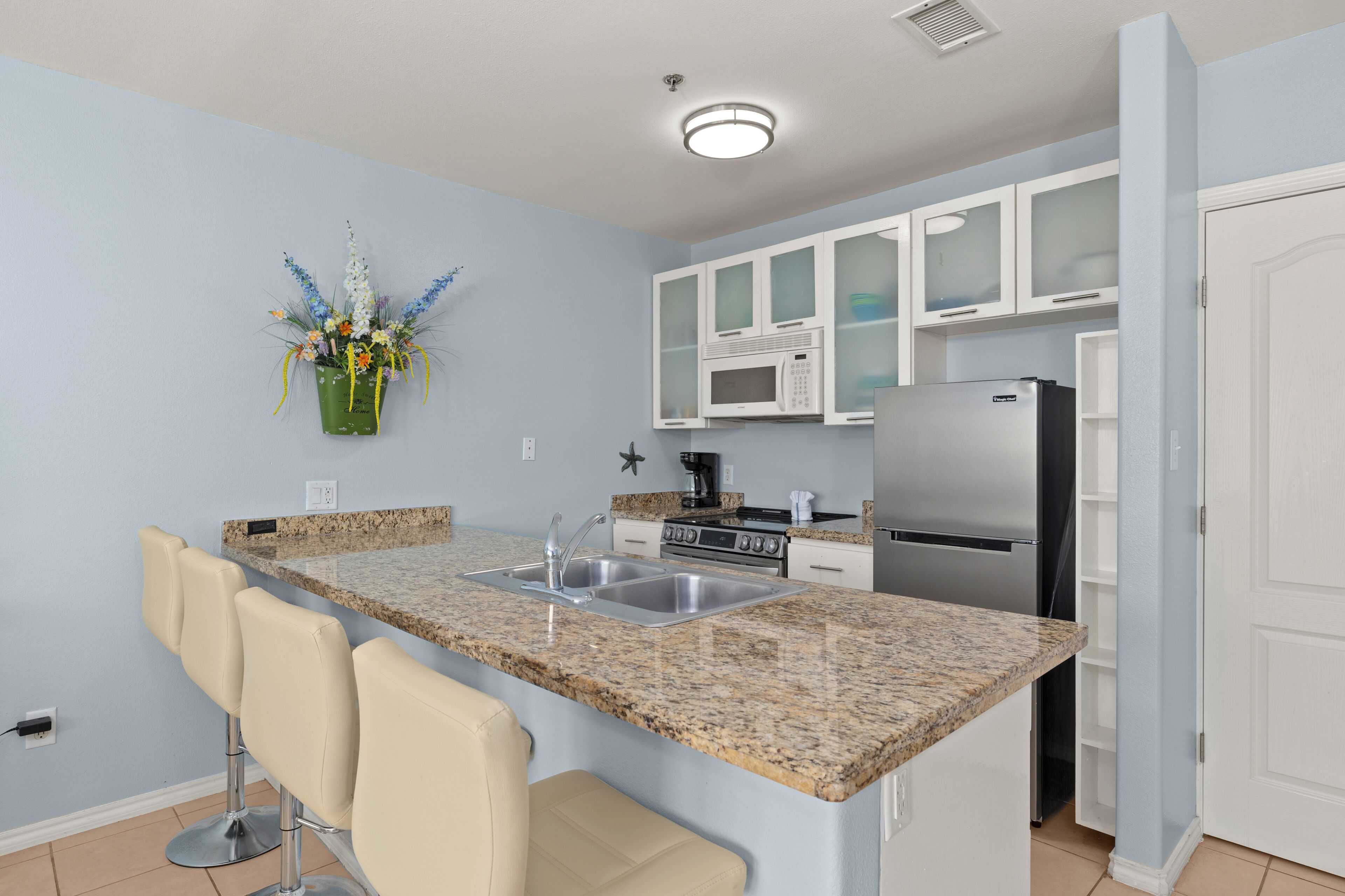 A kitchen with a granite countertop, stainless steel appliances, white cabinets, and a bar stool.