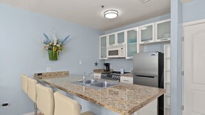 A kitchen with a granite countertop, stainless steel appliances, white cabinets, and a bar stool.