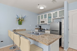 A kitchen with a granite countertop, stainless steel appliances, white cabinets, and a bar stool. - Seaside Cottage 107 just a 5 minute walk to the beach! (South Padre Island)