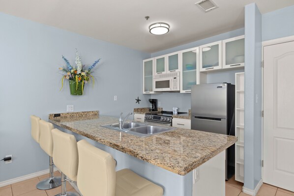 A kitchen with a granite countertop, stainless steel appliances, white cabinets, and a bar stool.