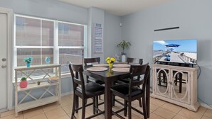 A dining area with a table, chairs, a TV, and a window with blinds.