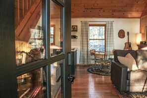 A cozy living room with a wooden floor, a leather sofa, a dining table with chairs, and a window with curtains.