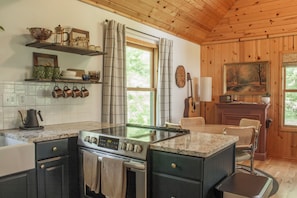 A kitchen with a central island, wooden cabinets, a stove, and a dining area with a chair and table.
