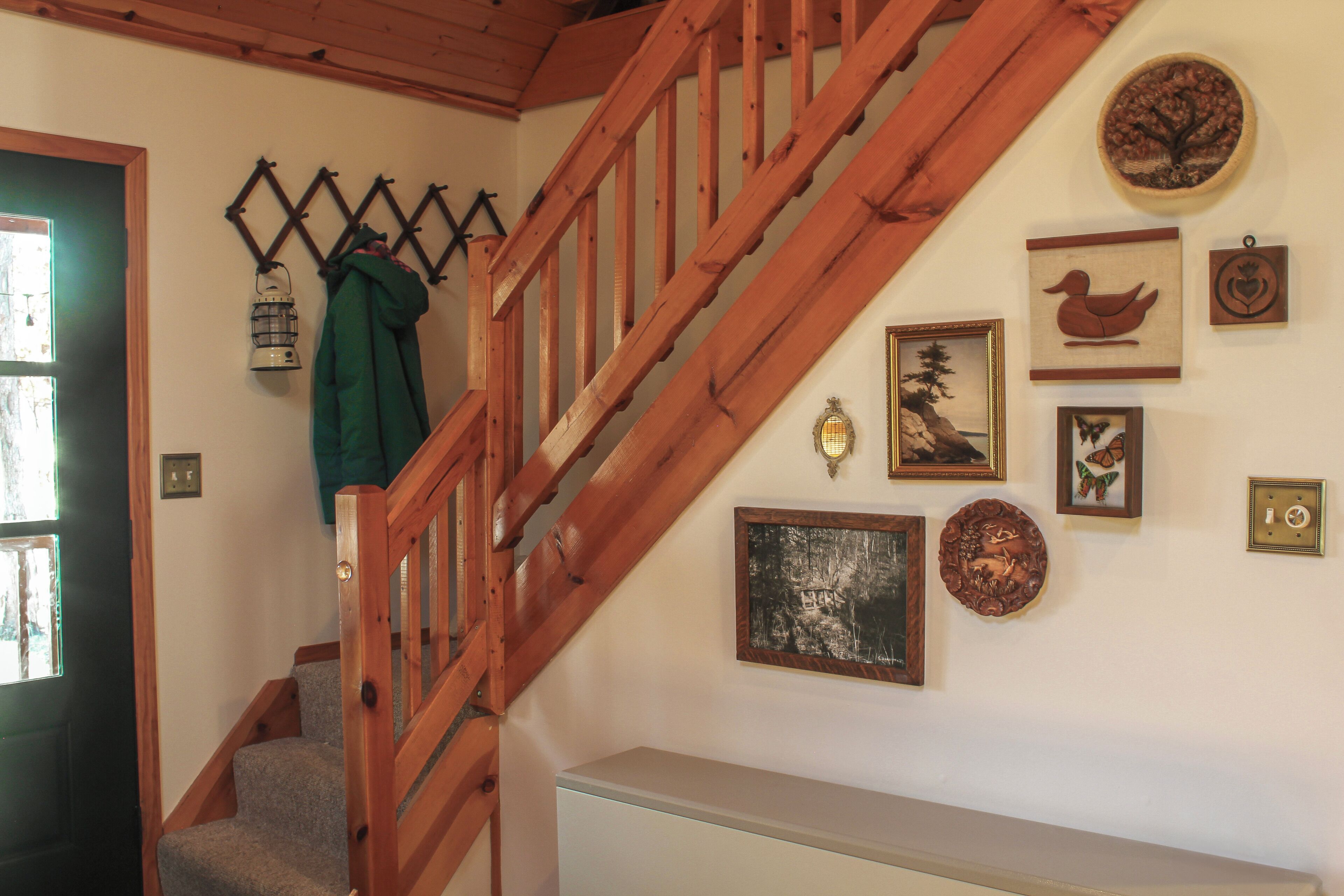 A wooden staircase with a handrail, a coat hanging on the wall, and various framed pictures and decorations.