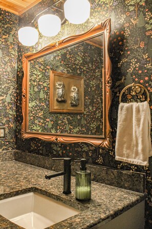 Une salle de bain avec un papier peint à motifs floraux, un grand miroir, un lavabo avec un robinet et un porte-serviettes.