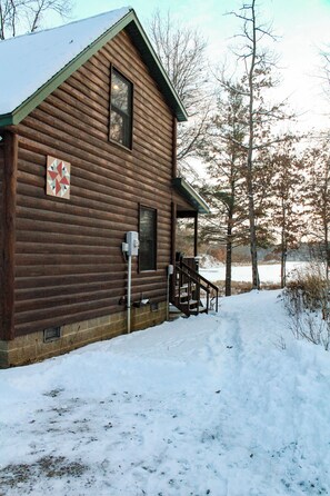 A wooden cabin with a covered porch and a snow-covered ground. - Lakeside Log Cabin + Hot Tub (Danbury)